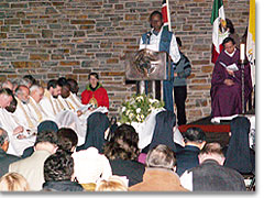 Lesung  in Englisch; im Hintergrund sieht man Priester aus allen Erdteilen